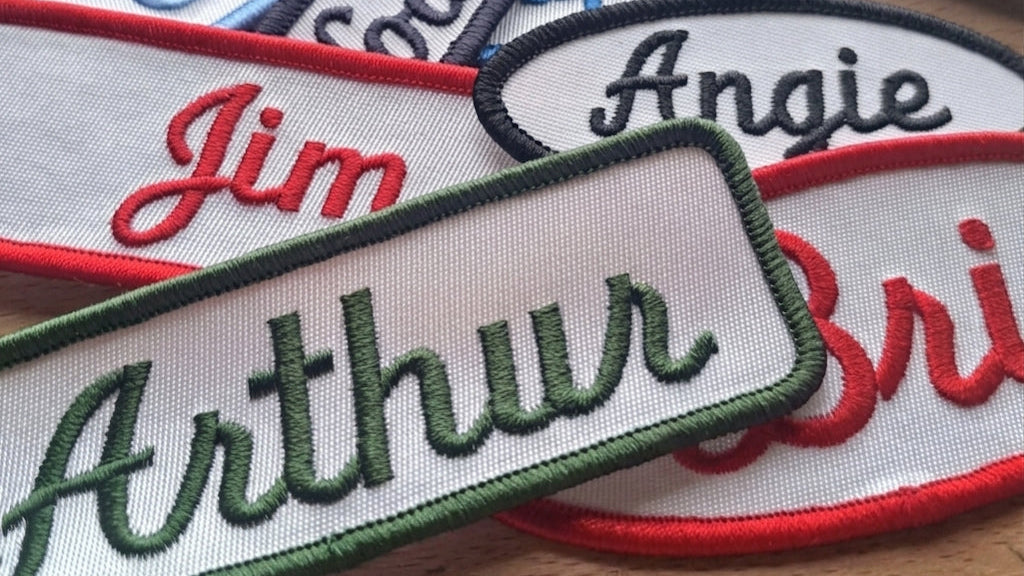 Embroidered name patches with various names on a wooden surface.   Made in Canada