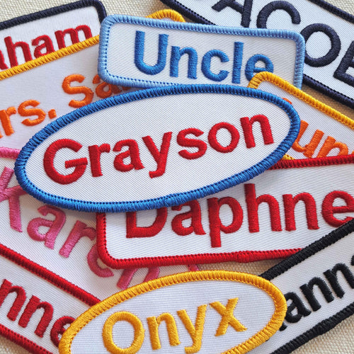 Collection of block font, embroidered name patches with various names on a textured surface.